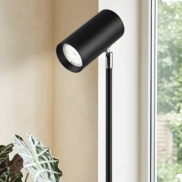 Black floor grow light with adjustable head in a room with a window and plant