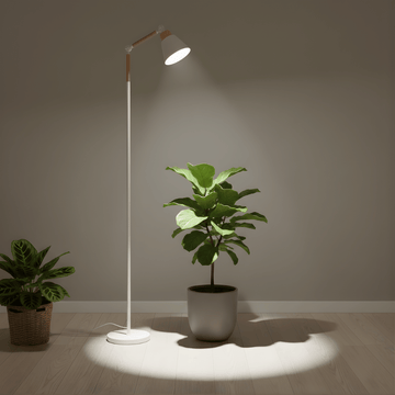 Floor grow light illuminating a potted plant in a room with a neutral wall and wooden floor.